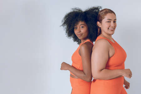 multiethnic beautiful young hispanic latina girls, posing with their backs together, looking at camera, wearing orange sportswear on a white background. image with copy space.の写真素材
