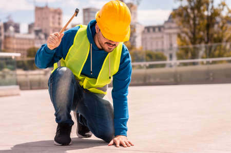 latin male worker with yellow hard hat, glasses and green vest with hammer in hand