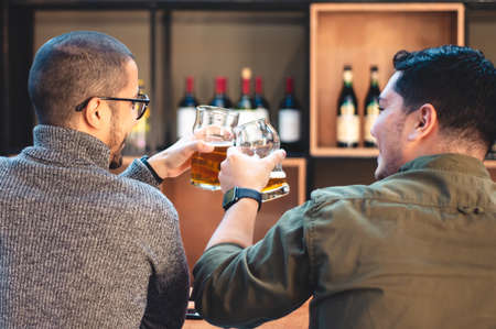 two young latin guys, enjoying smiling and talking to each other, making a toast with craft beer,...