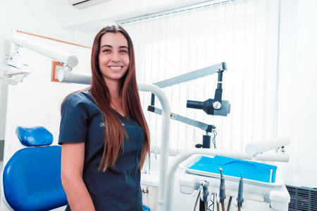 pretty young white skinned latina girl and professional dentist in her dental office, standing at the side of the dental chair, ready to start her consultations and routine checkups. dental clinic concept.の写真素材