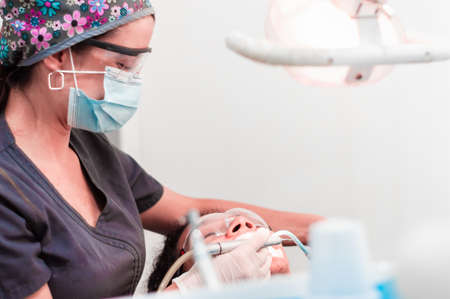 pretty professional dentist girl doing a dental cleaning to a boy sitting upright in the dental chair and wearing protective plastic glasses. dental clinic concept.の写真素材