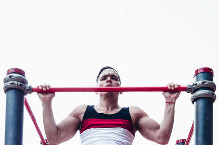 young athletic latin athlete, white skin, doing pull-ups, with the sky in the background, in a fitness plaza, outdoors.の写真素材