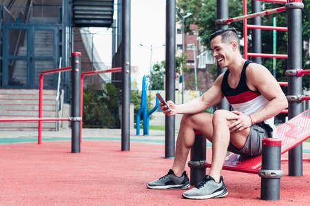 young, athletic, white-skinned latino athlete, sitting, talking on the phone in a fitness center, outdoors.の写真素材