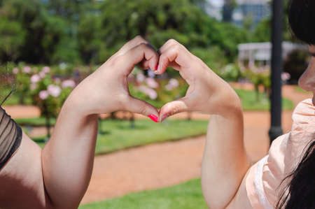 two caucasian girls outside in a park making a heart of love and friendship with their hands, valentines day concept.の写真素材