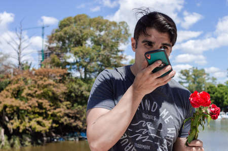 young caucasian hispanic latino man on a bridge in a public park, with a flower in his hand sending...