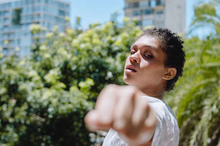profile view of young brunette argentine hispanic latin woman with short hair, extending her fist and looking at camera, inclusion, girl power and lifestyle concept.の写真素材