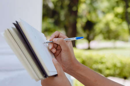 closeup of female hands holding a notebook and making notes with a pen outdoors in a park, image with copy space.の写真素材