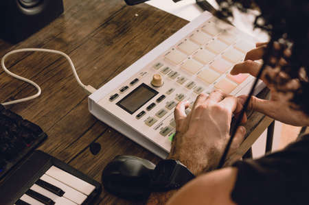 rear view of caucasian man making beats on a midi controller in his home studio, producing...