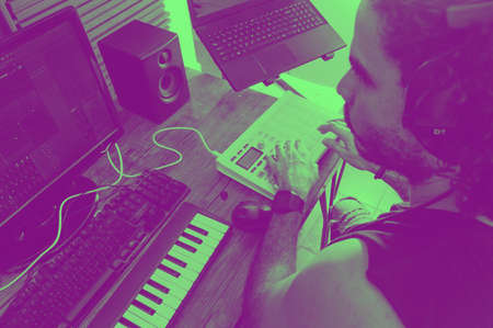 caucasian male music producer watching computer monitor working in home studio with keyboard, making compositions with midi controller.の写真素材