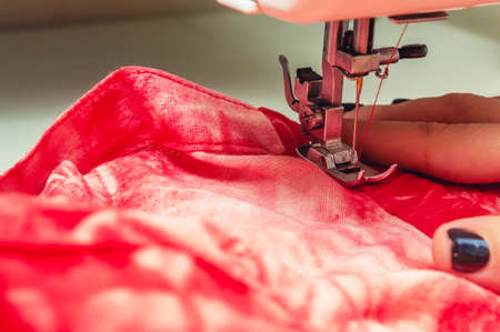 closeup of sewing machine needle sewing a red fabric with red thread with copy space, detail of...