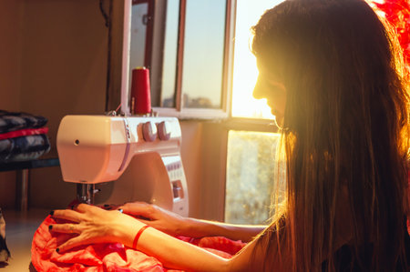 Portrait of a young Caucasian Argentine woman sitting by the window working with a sewing machine,...