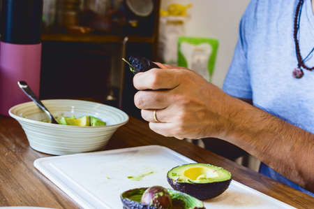 closeup caucasian man sitting in his kitchen chopping avocado to prepare guacamole for lunch.