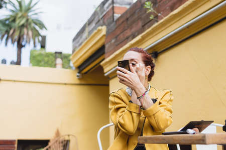 young argentinian caucasian woman sitting putting on makeup in the backyard looking at herself in a...