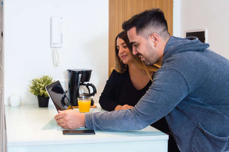 Caucasian young heterosexual couple using laptop at home, leaning on counter watching screen, buying household items online.の写真素材