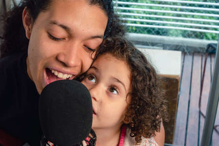 closeup latin caucasian father and daughter with curlers singing happily with a microphone indoors...