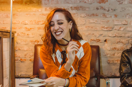 beautiful young caucasian woman sitting with her eyes closed in a restaurant smiling and making notes in her notebook and a pen.の写真素材
