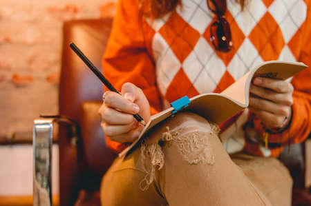 closeup unrecognizable caucasian woman writing notes with a pencil in her notebook on her leg,...