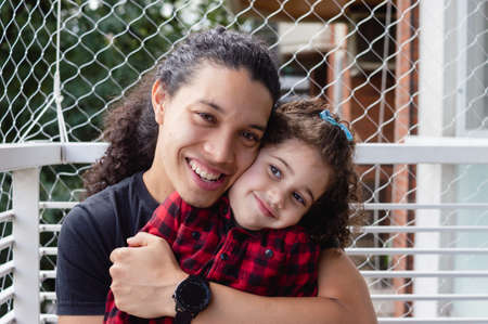 portrait young caucasian venezuelan father and daughter with curly hair smiling outside on the apartment balcony looking at the cameraの写真素材