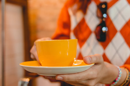 closeup caucasian woman holding a yellow coffee cup in a restaurant, blurred background with copy...