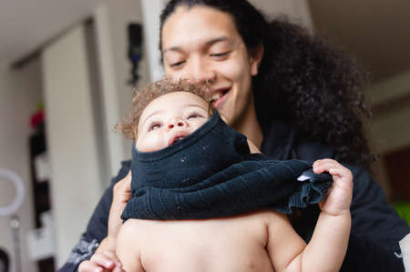 young father at home helps his daughter with the clothes, he is putting a sweater on her and it got...