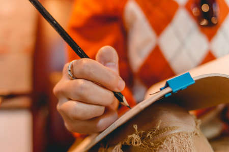 closeup of female caucasian hand writing in a notebook with a black pencilの写真素材