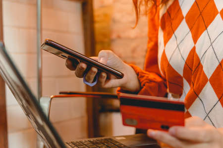 closeup young woman shopping online with laptop, phone and credit card, focus on phone.