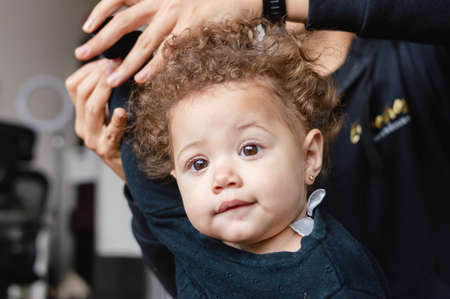 portrait little baby looking forward in the living room while her father behind her finishes putting on a sweater.の写真素材