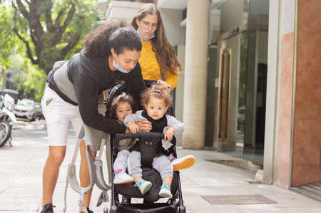 young caucasian man standing in the street with his family taking his daughter out of the baby car,...