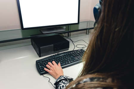 rear view of female call center worker sitting in front of computer, watching screen with one hand on keyboard, technology concept with copy space.の写真素材