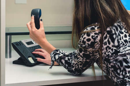 rear view unrecognizable young woman in office dialing on the phone lying on the desk calling her clients holding the headset.の写真素材