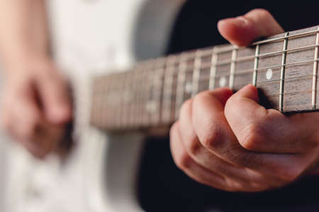 close up caucasian male hand playing white electric guitar making a chord, focus on left hand, music...
