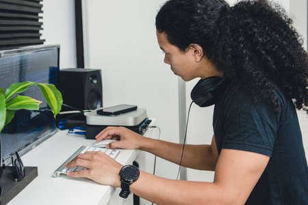 Concentrated long-haired young Caucasian man working in his home music studio, producing, mixing and...