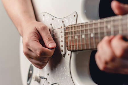 close up unrecognizable caucasian man playing electric guitar with plectrum, focus on right hand,...