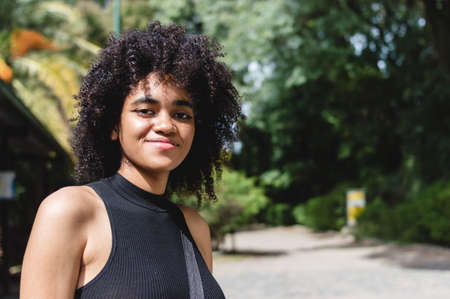 portrait young brunette woman with afro on vacation outdoors in a natural park, looking at the camera smiling.の写真素材