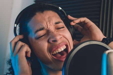 young caucasian singer man recording voice with condenser microphone and headphones inside in...