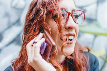 close up beautiful young redhead woman with glasses, outdoors talking on the phone and laughing.の写真素材