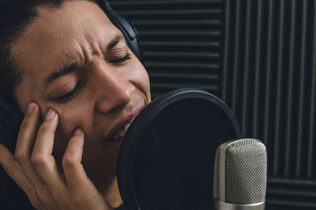 close up portrait man recording song in music studio, using condenser microphone inside chamber with acoustic treatment, copy space.の写真素材