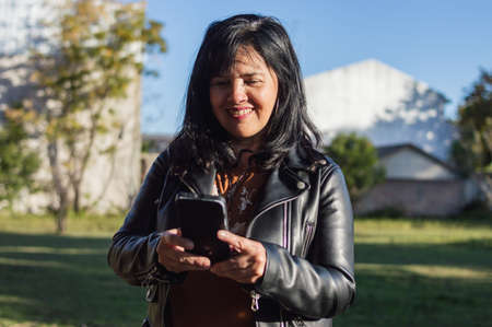mature latin caucasian woman on the farm, outdoors smiling and texting on her phone, wearing black...