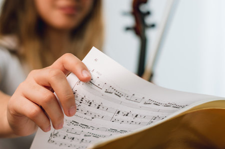 close up hand of a female violinist changing the page of the sheet music on the music stand. focus on hand. blurry woman in background with copy space.の写真素材