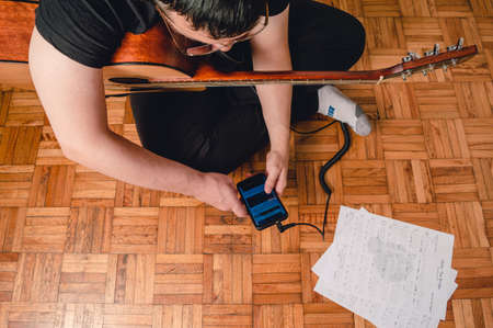 top view young caucasian man sitting on the floor with an acoustic guitar studying music with sheet...