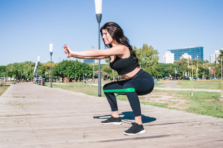 Sporty and active latin caucasian young woman outdoors, crouching concentrated training leg muscles...