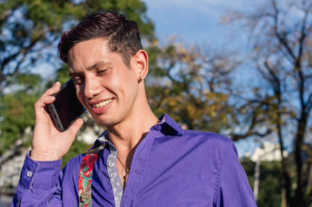caucasian young latin man outdoors on a sunny day, wearing purple casual clothes, smiling and...