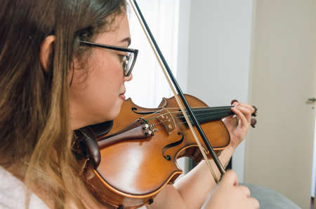 side view young latin caucasian venezuelan woman, playing the violin, practicing classical music at home. close up view with copy space.の写真素材
