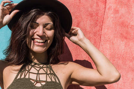 portrait beautiful young latin caucasian woman, outdoors standing with red wall behind her, smiling with eyes closed and wearing a hat, cup space. lifestyle concept.の写真素材
