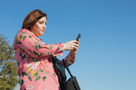 young latin caucasian woman outdoors calling a taxi by mobile app after shopping, copy space