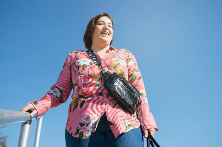 Laughing latin argentinian caucasian young woman hold handrail of stairs in street, happy going downstairs to go shopping.の写真素材