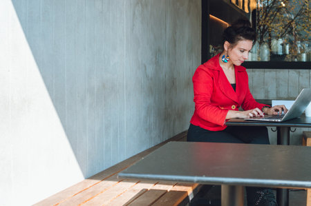 side view with copy space of young caucasian business woman, wearing red casual clothes, sitting in a restaurant, working with her laptop.の写真素材