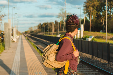 Caucasian young woman with a half-shaven head and curlers with a backpack standing on the station...