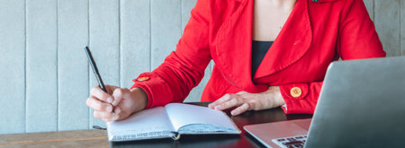 banner of unrecognizable caucasian adult woman dressed in a red blazer, she is sitting making notes...