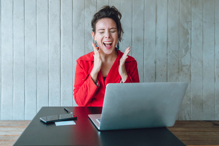 adult caucasian business woman with her laptop screaming with joy for her profit and the sales of her products online, sitting in a restaurant working.の写真素材